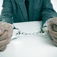 Trouble In Our State Government a man wearing a suit sitting in a desk, with handcuffs in his wrists