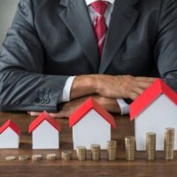 businessman with different size houses and stacks of coins on table