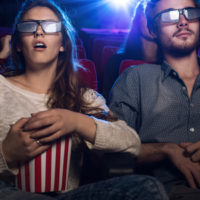 young teenagers at the cinema wearing glasses and watching a 3d movie, a girl is eating popcorn, entertainment and movies concept