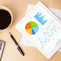 workplace with tablet pc showing charts and a cup of coffee on a wooden work table close-up