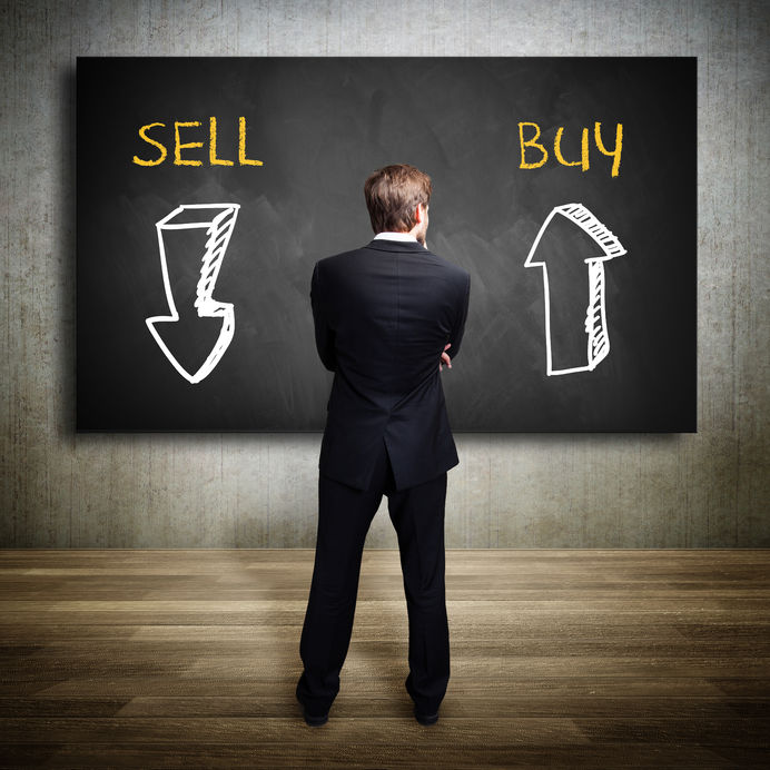 businessman standing in front of a blackboard trying to decide whether to buy or to sell