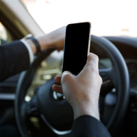 Man in suit driving car and holding mobile phone near the steering wheel