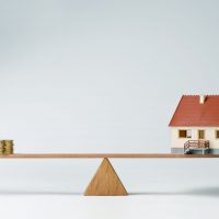 Model house and money coins balancing on a seesaw