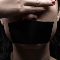 Concept on the topic of freedom of speech, censorship, freedom of press. International Human Right day: the girl's face is sealed her mouth with black paper
