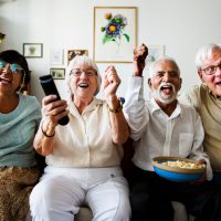 Group of cheerful senior friends sitting and watching TV together