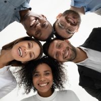 Close up vertical low angle portrait of smiling multiethnic diverse employees pose together look at camera laughing. Happy young multiracial workers friends have fun show unity. Diversity concept.